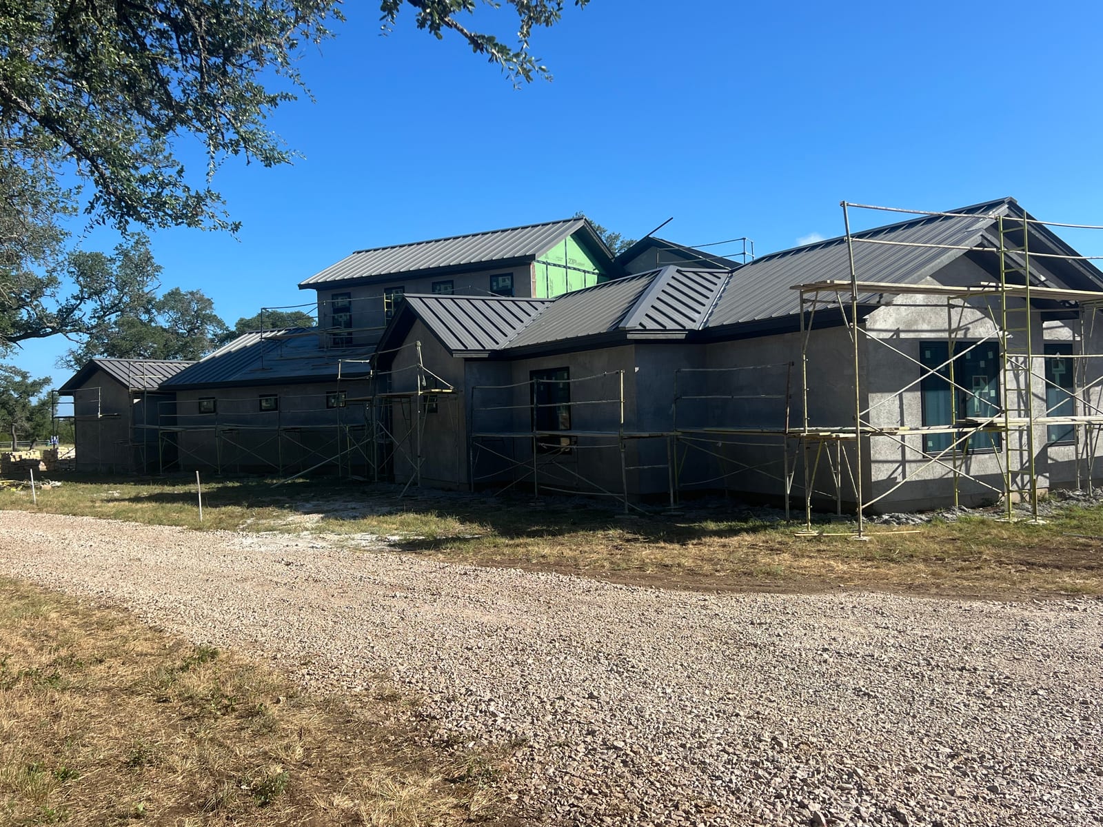 Dark standing seam metal roof covering several connected gables and wings of a large new stucco home, seams running clean from ridge to eave