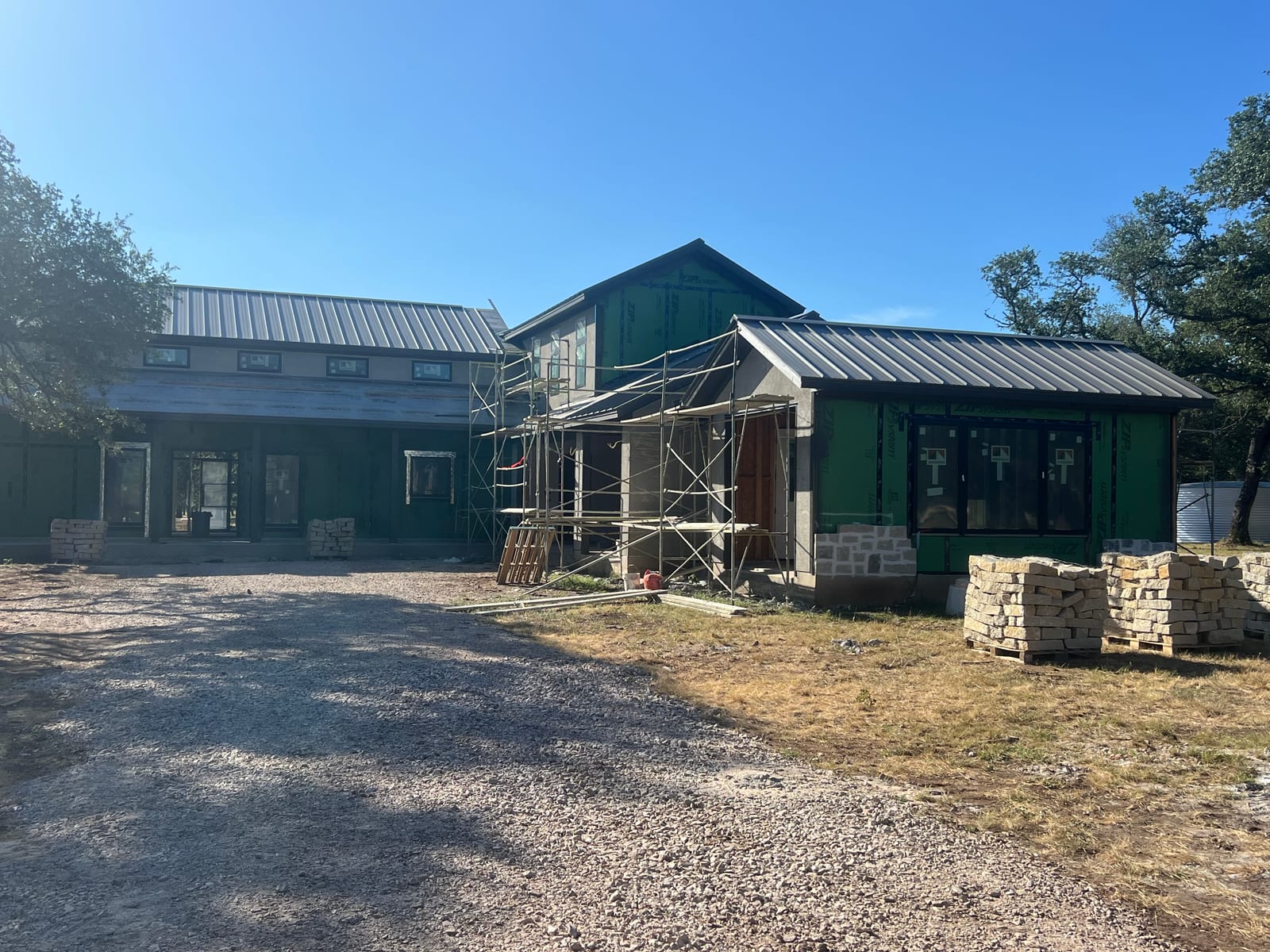 New home under construction with the dark metal roof already finished, scaffolding up and walls still in green sheathing
