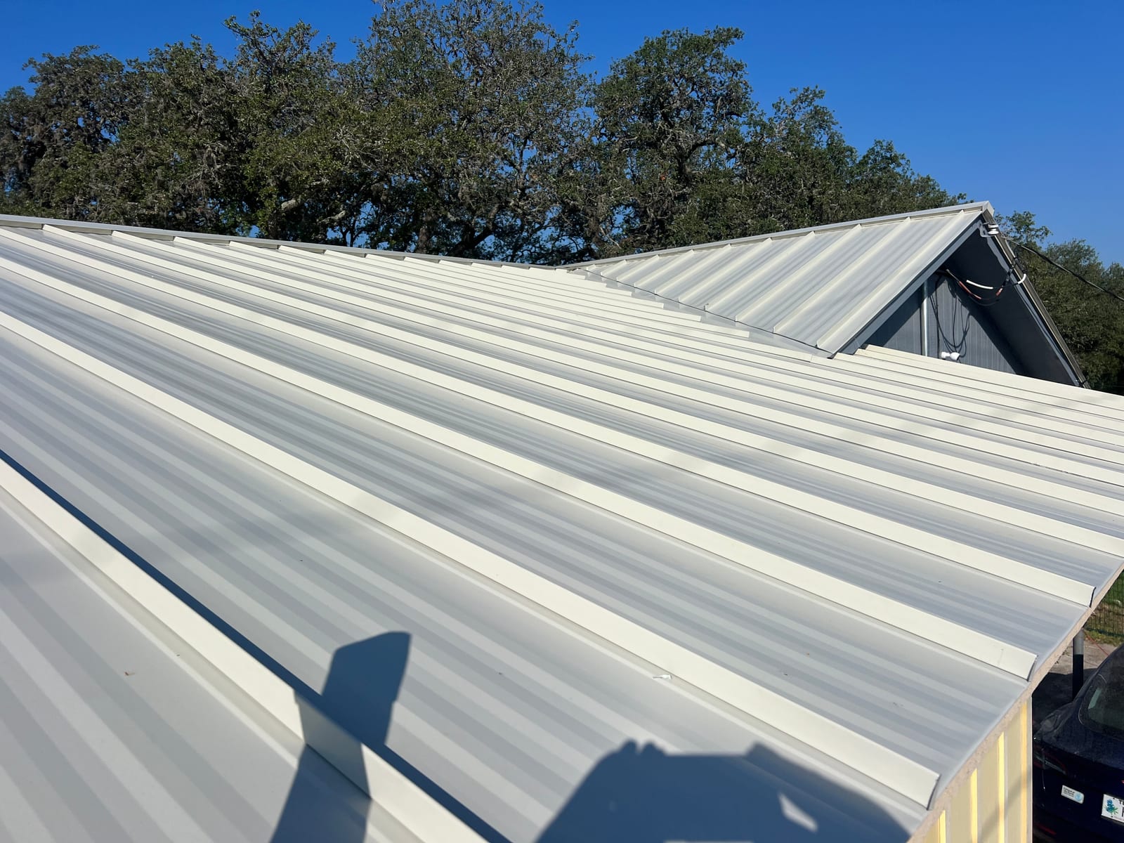 Finished standing seam metal roof in a light sandstone color, seams running unbroken up a wide plane to a clean hip against a blue sky