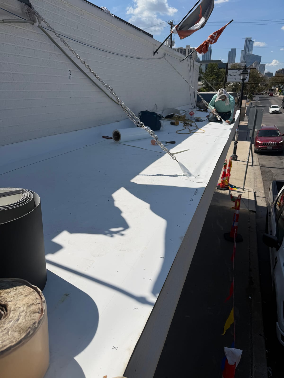 Roofer detailing the TPO membrane at the wall, with East 6th Street and the downtown skyline beyond