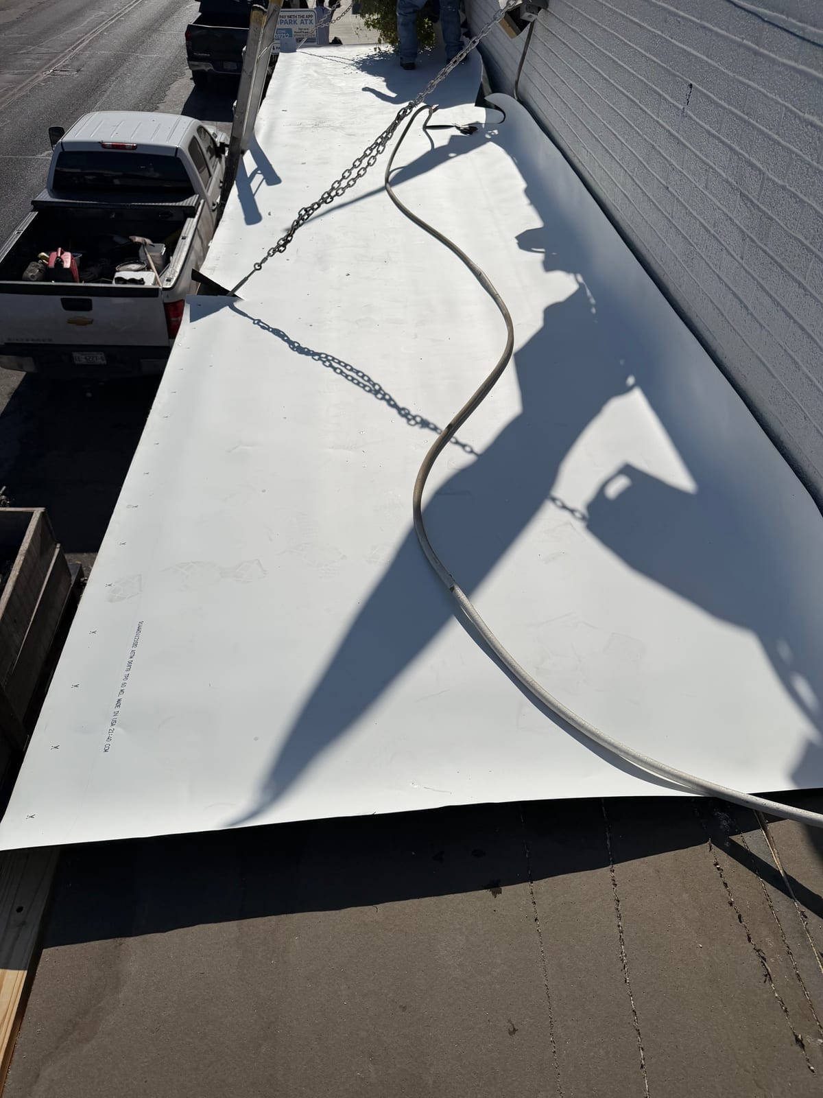 White TPO membrane being rolled out over the canopy roof alongside the brick wall