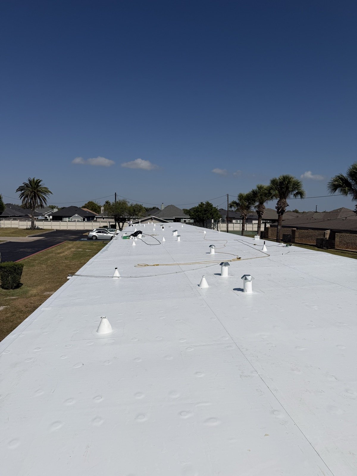 Completed bright white TPO roof with sealed penetration boots under a clear sky