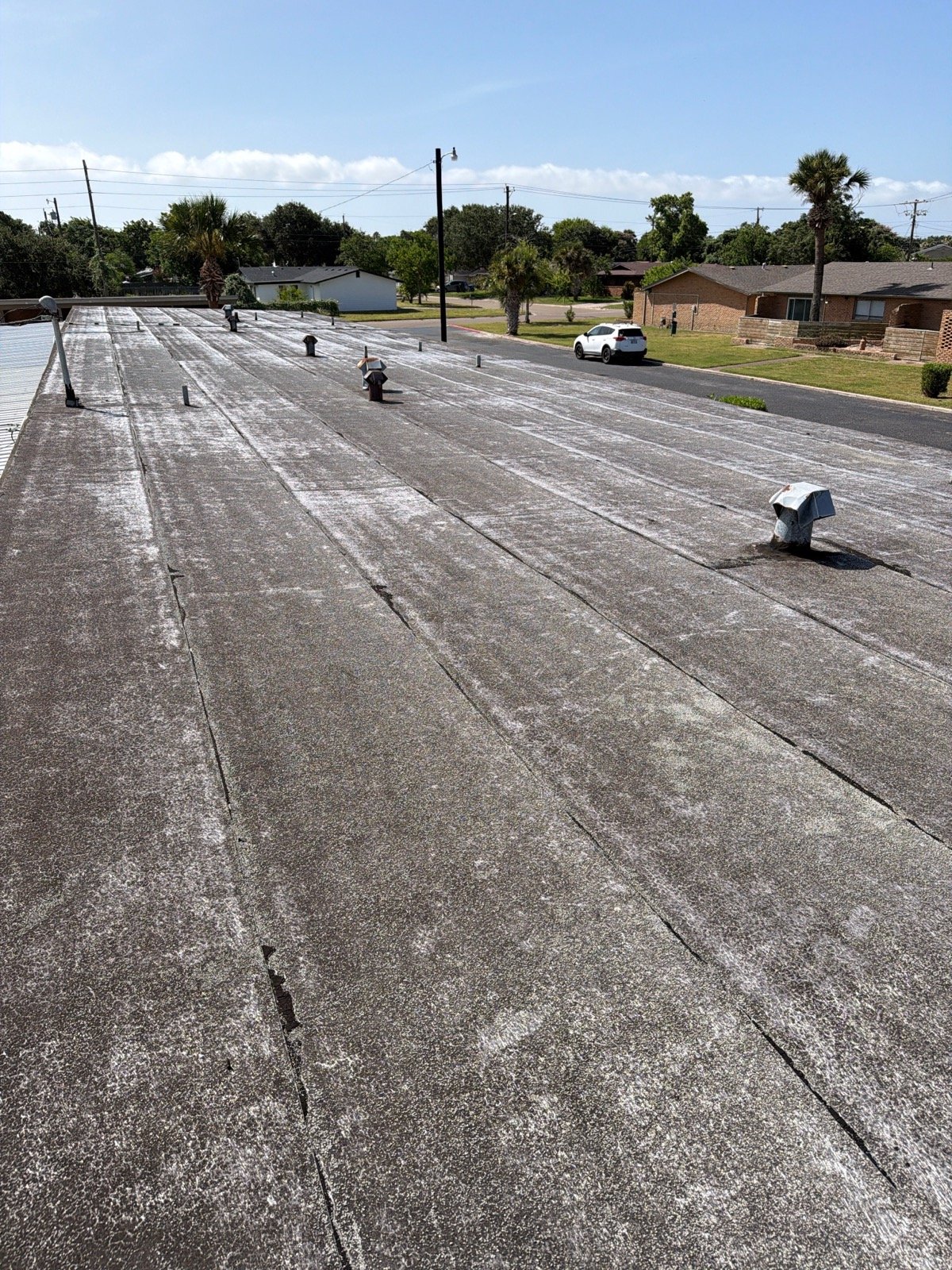 Weathered modified bitumen roof with granule loss across a long low-slope building