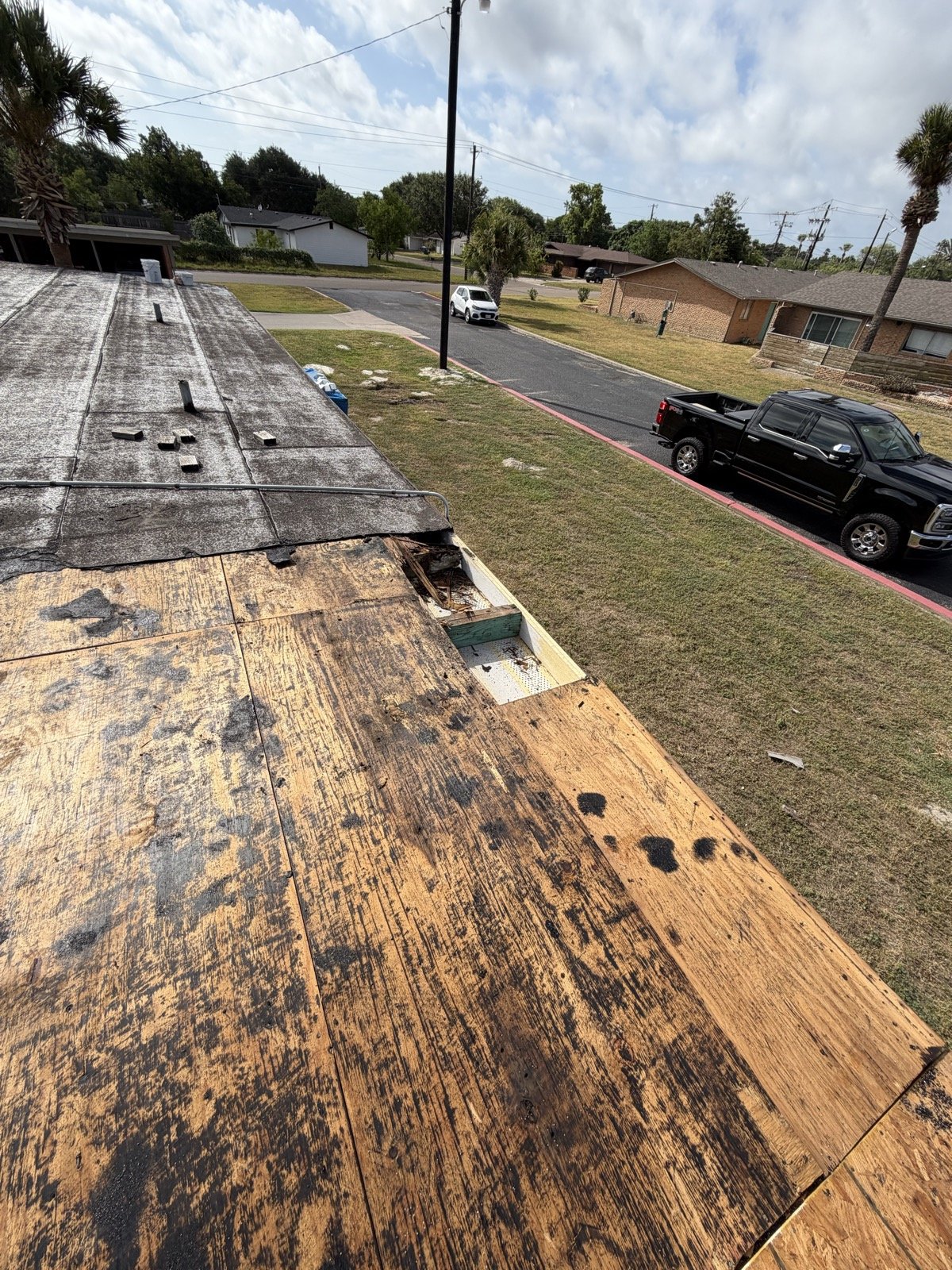 Tear-off in progress with old roofing removed and stained plywood decking exposed