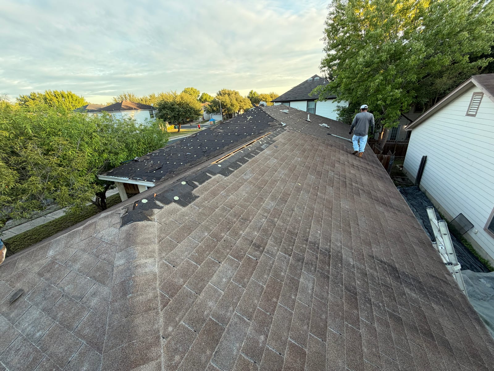 Worn brown shingle roof on a single-story home with the first course of tear-off started along the far slope