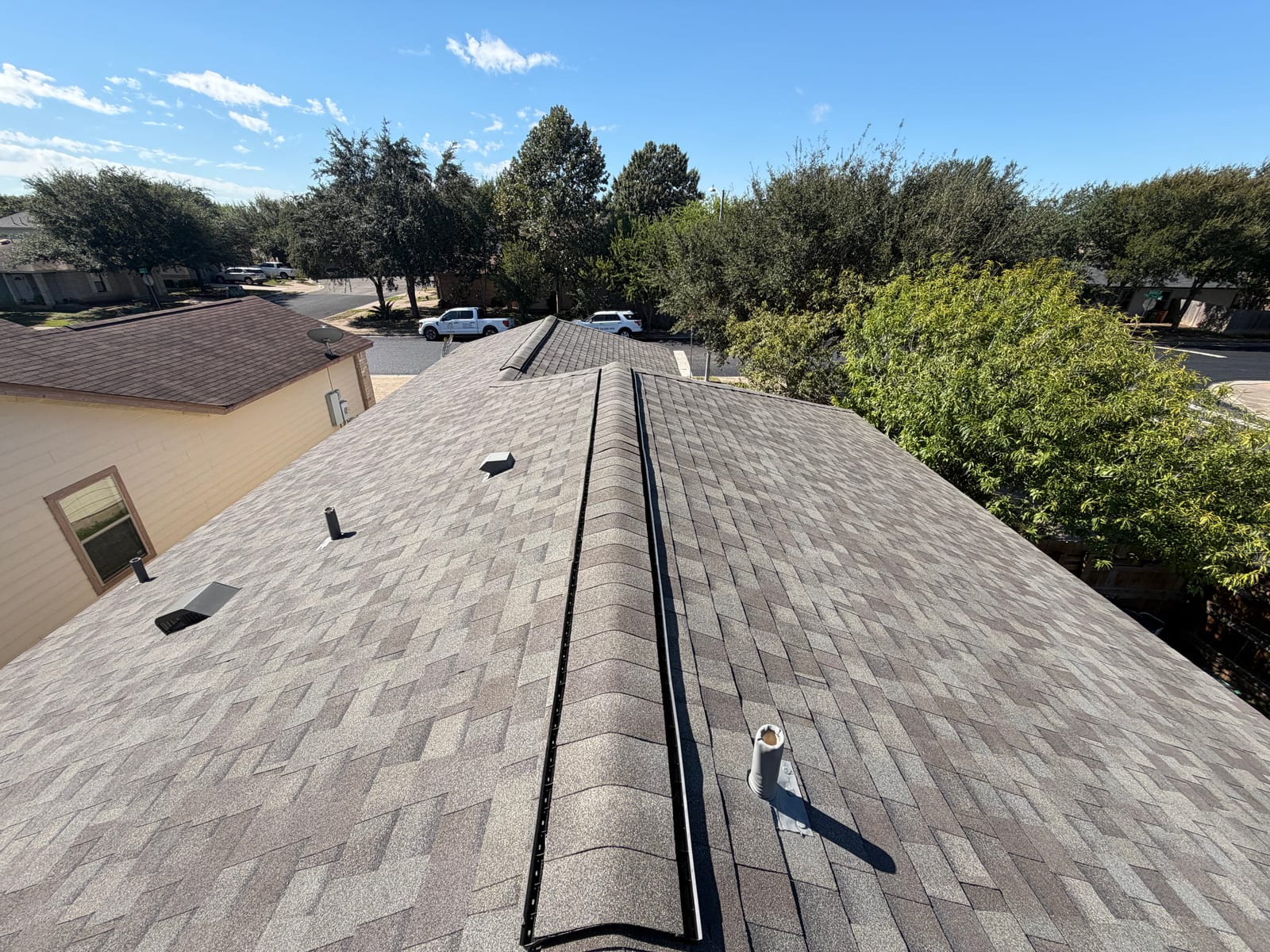 Close view along the ridge showing the continuous ridge vent capped with matching shingles and a new pipe boot in the field