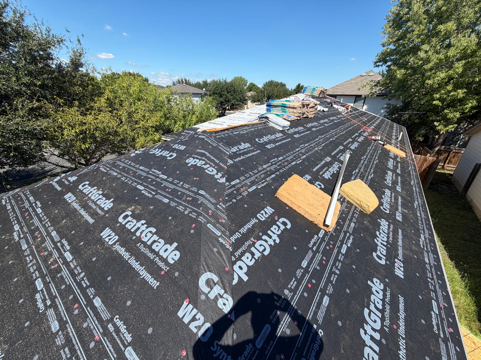 Synthetic underlayment covering the roof deck with bundles of new shingles stacked along the ridge