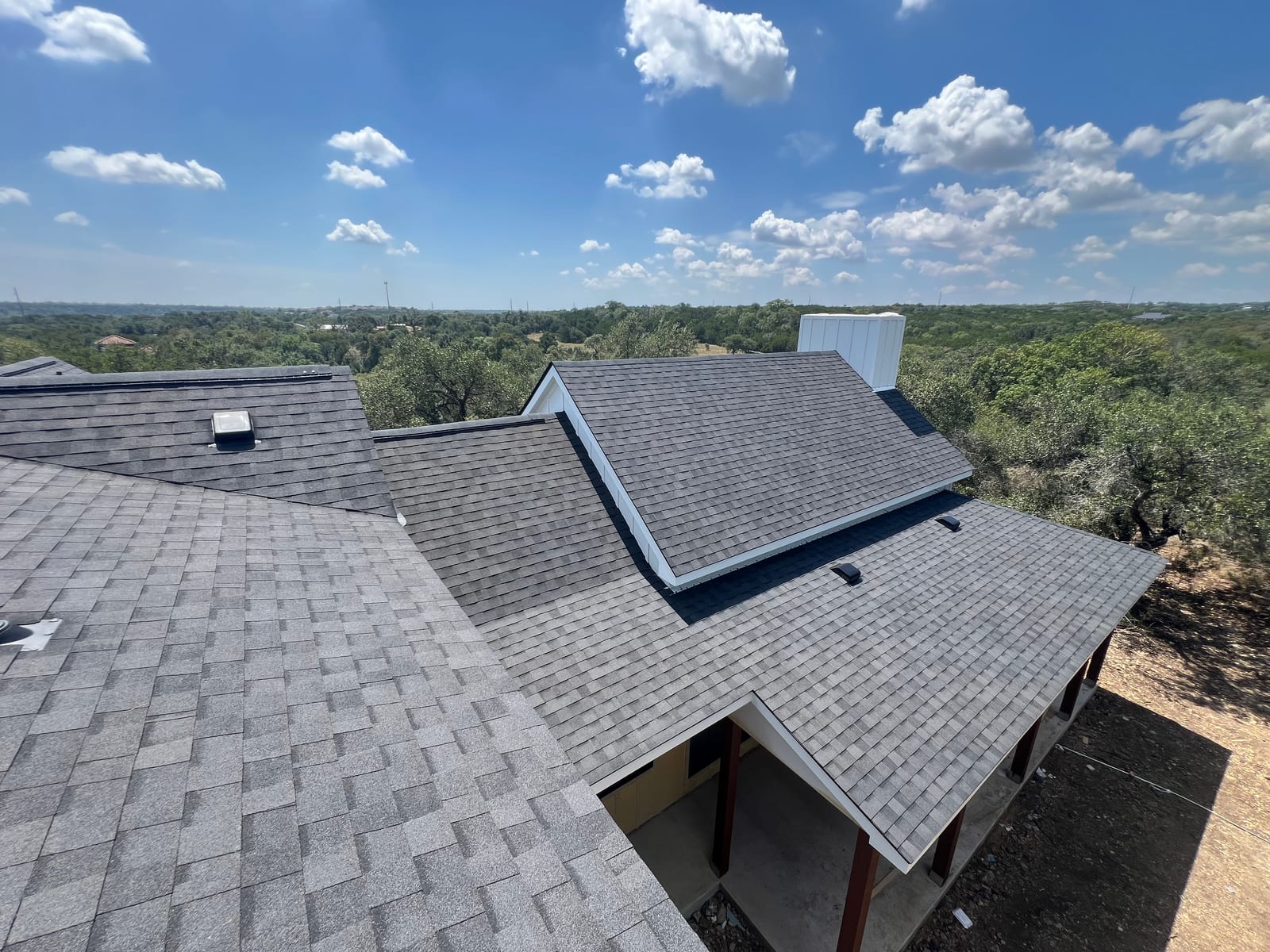 Completed architectural shingle roof on a custom home, dormer and porch roofs below a wide Hill Country sky