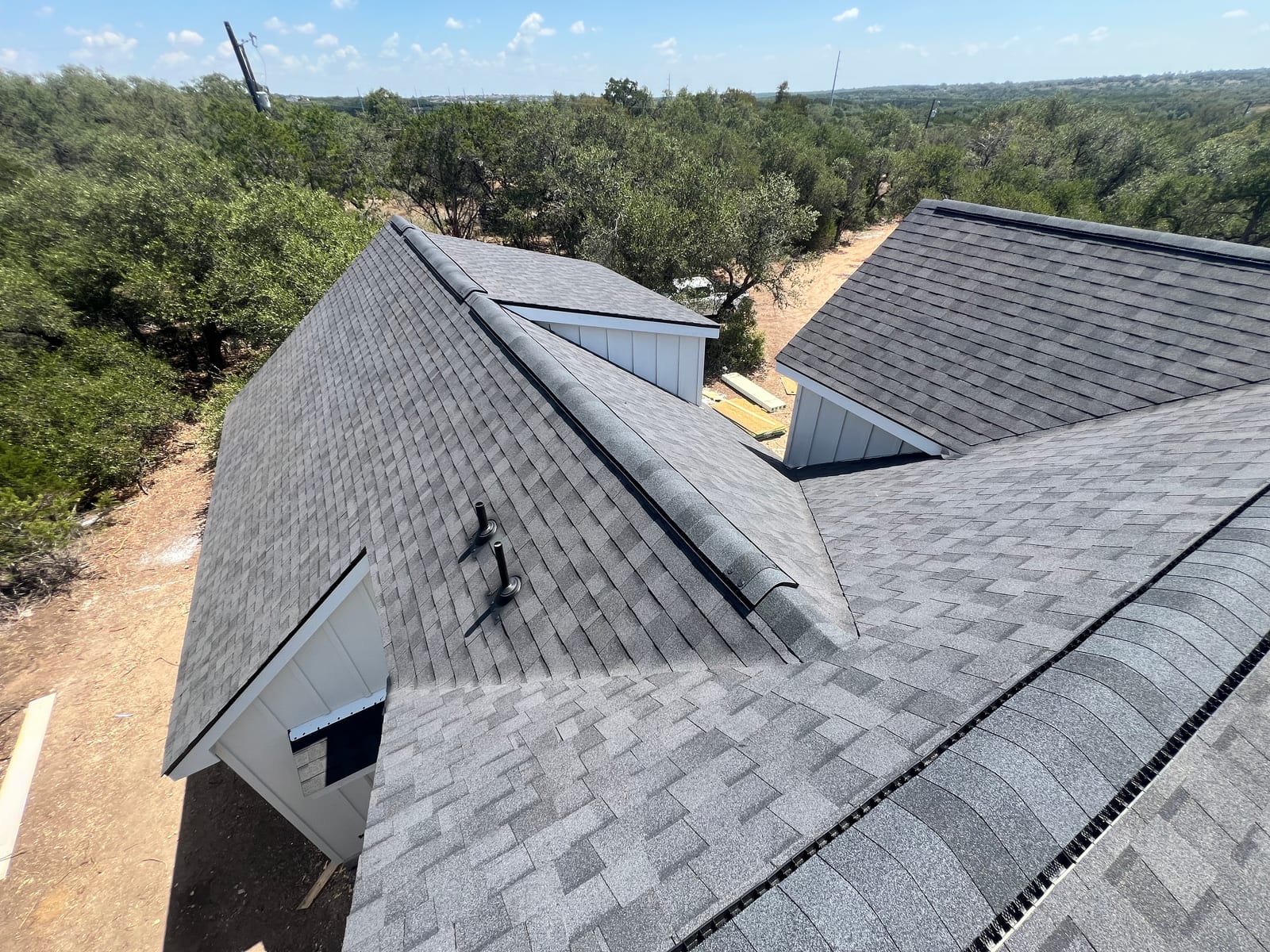 Aerial view down onto several planes of a new shingle roof where hips and valleys meet around a dormer