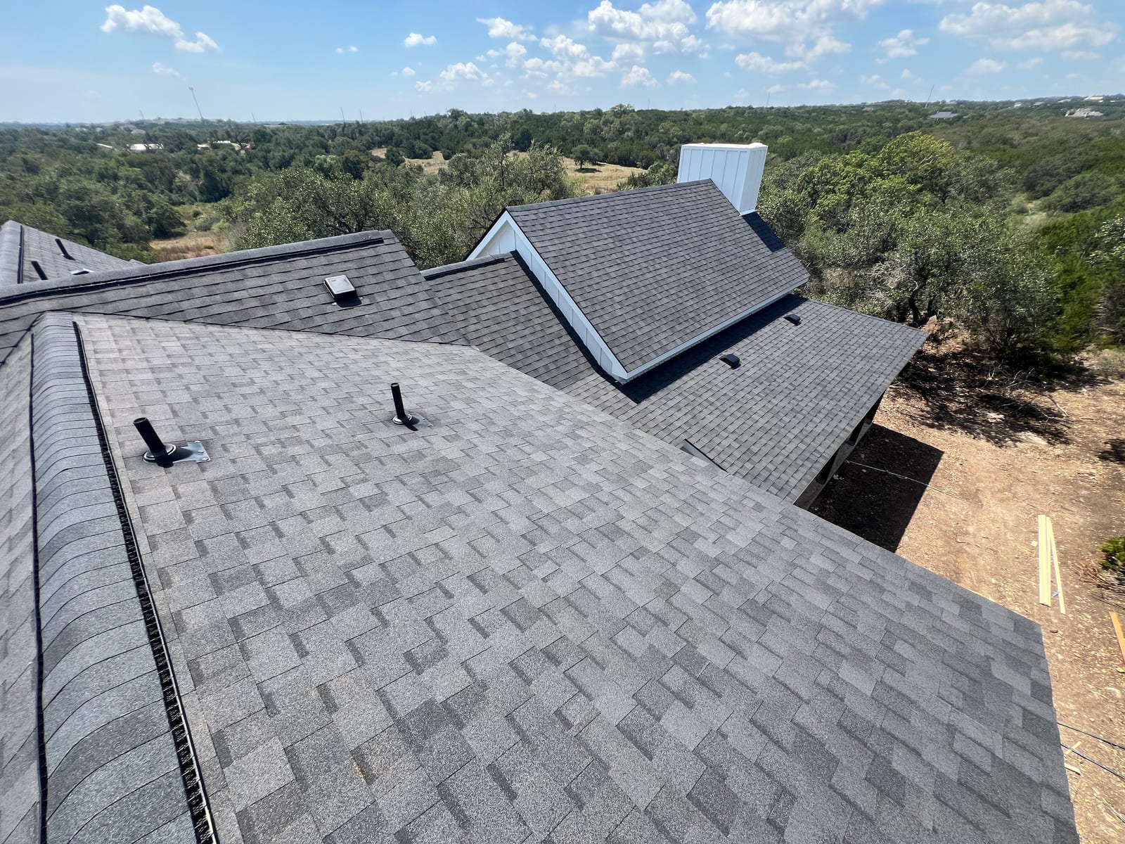 New architectural shingles running across a broad roof plane toward dormers and tree cover beyond