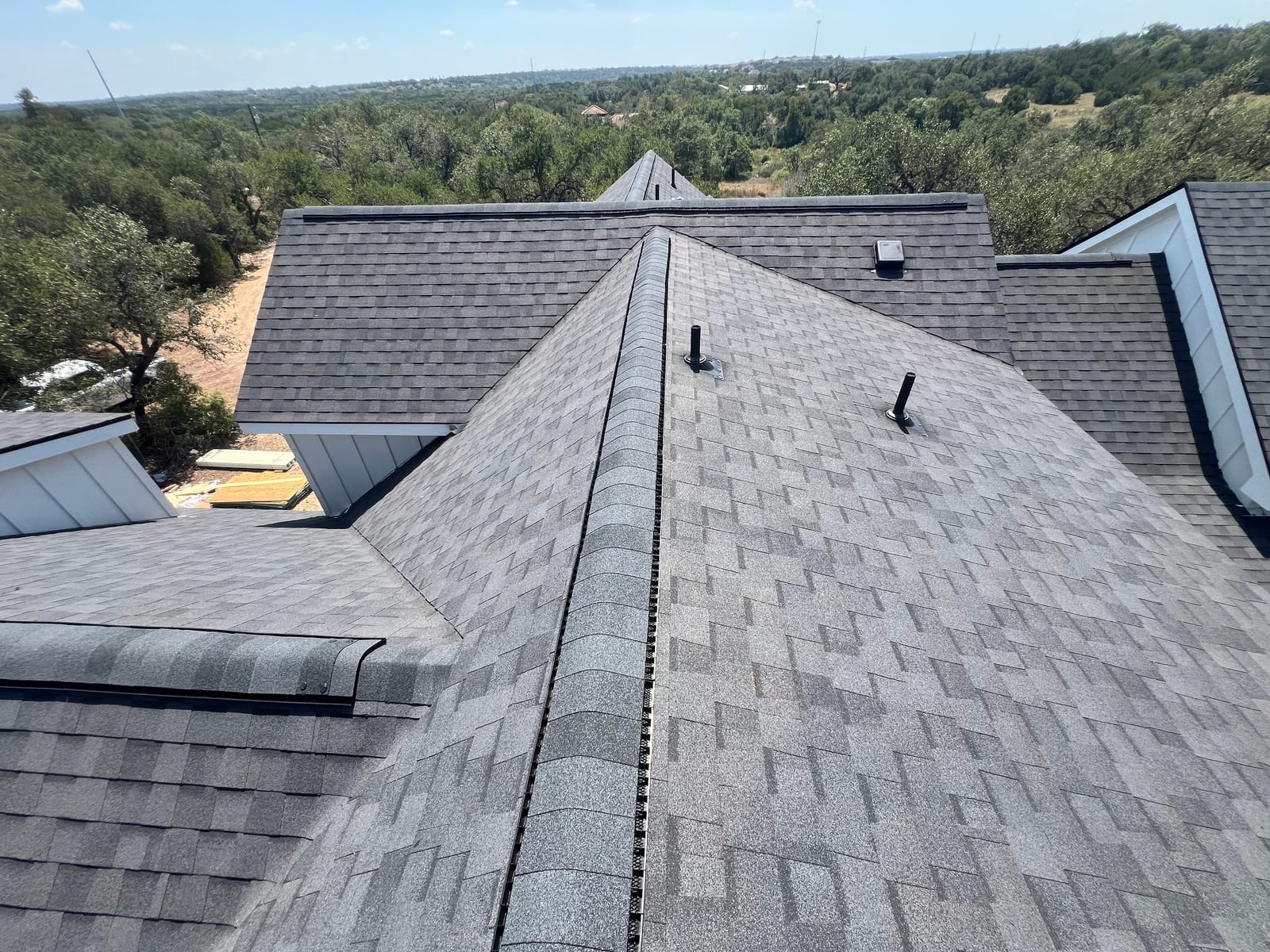 View along a roof ridge showing continuous ridge vent capped with matching shingles and painted pipe boots in the field
