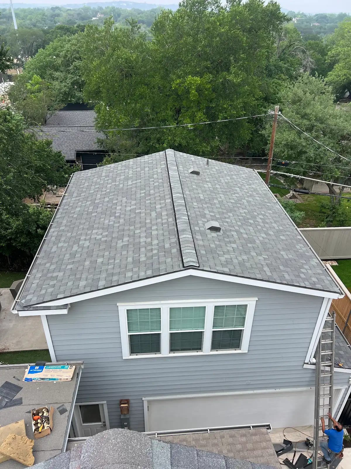 Two-story home with a newly shingled upper roof and CertainTeed Landmark bundles staged below